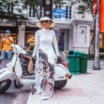 Stylish woman in ao dai standing next to a Vespa scooter in Vietnam, capturing a blend of tradition and modern style.