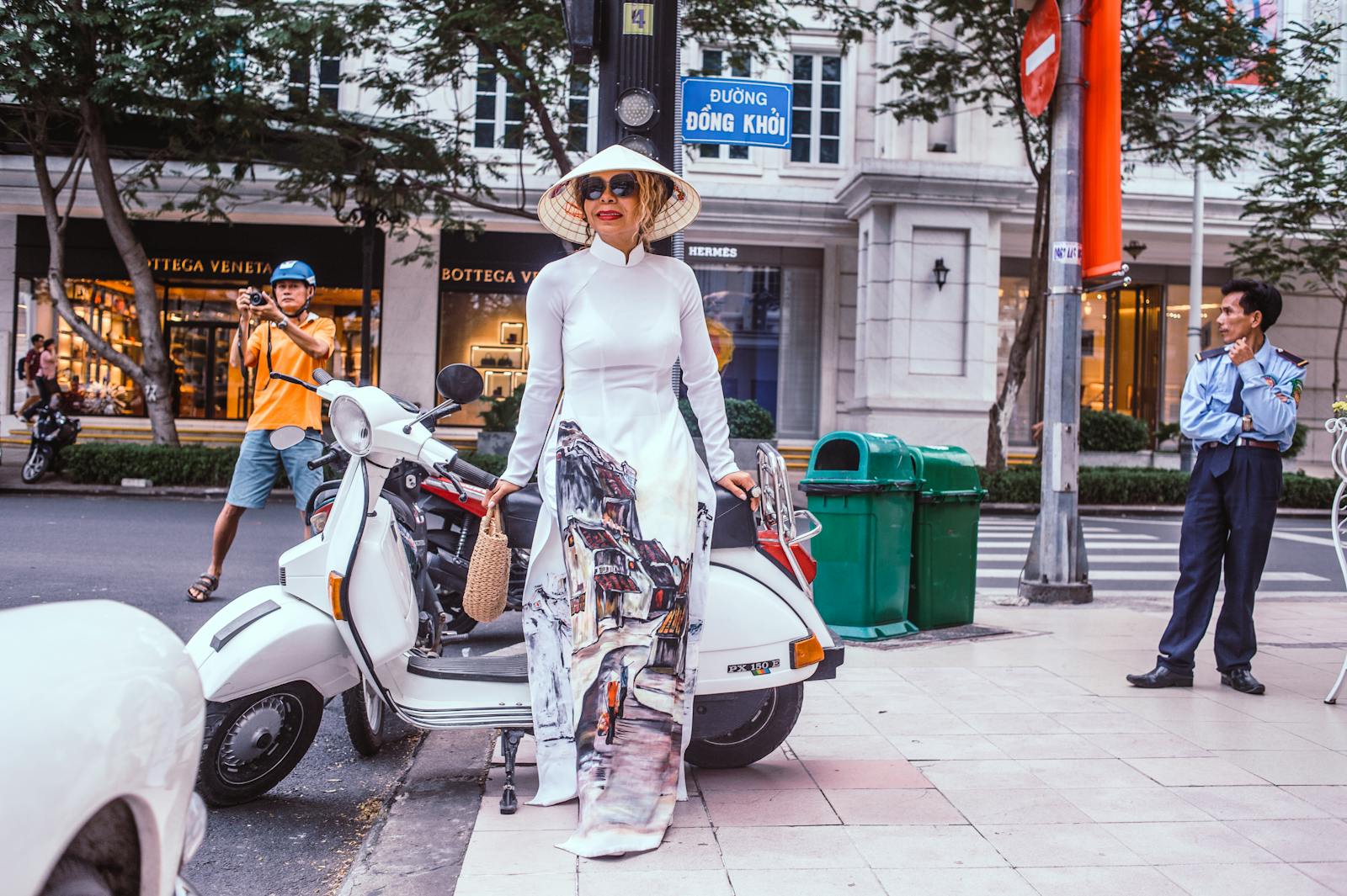 Stylish woman in ao dai standing next to a Vespa scooter in Vietnam, capturing a blend of tradition and modern style.