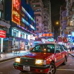 Bustling Hong Kong street at night with neon lights and red taxi, epitomizing urban life.