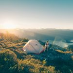 man sitting on stone beside white camping tent